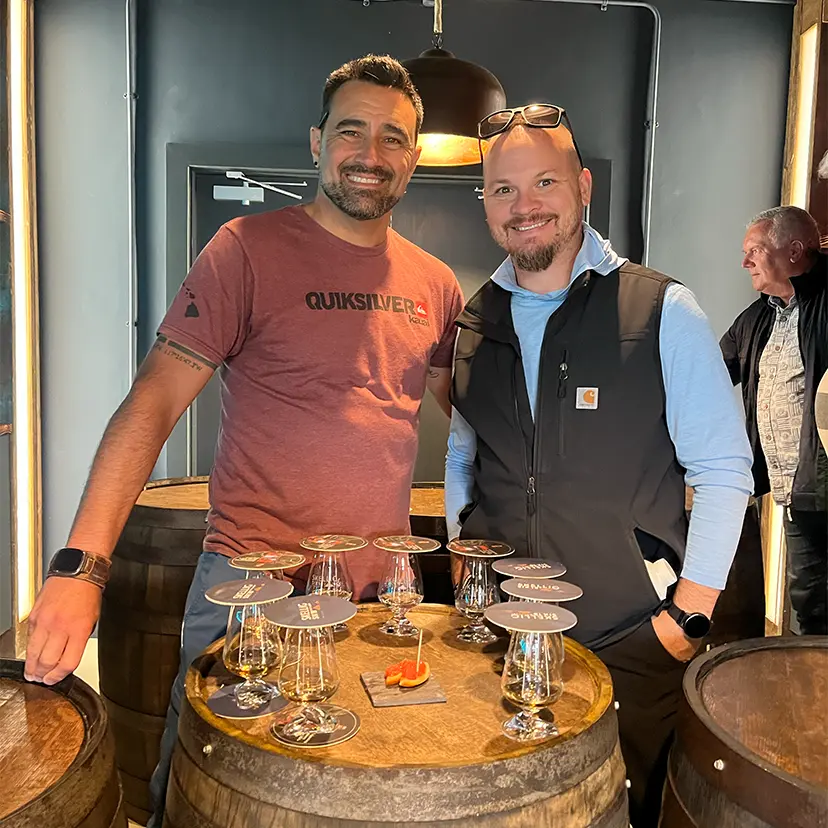 Men standing in front of a barrel with whiskey samples on it